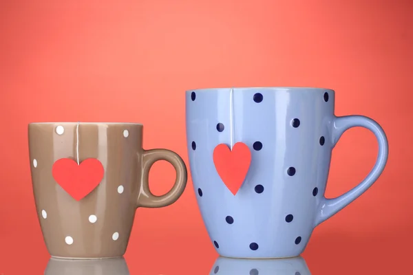 Duas xícaras e sacos de chá com rótulo vermelho em forma de coração no fundo vermelho — Fotografia de Stock