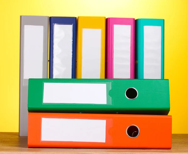 Bright office folders on wooden table on yellow background — Stock Photo, Image