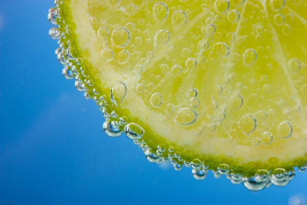 Slice of lemon in the blue water with bubbles — Stock Photo, Image