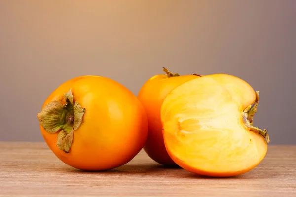 stock image Appetizing persimmons on wooden table on grey background