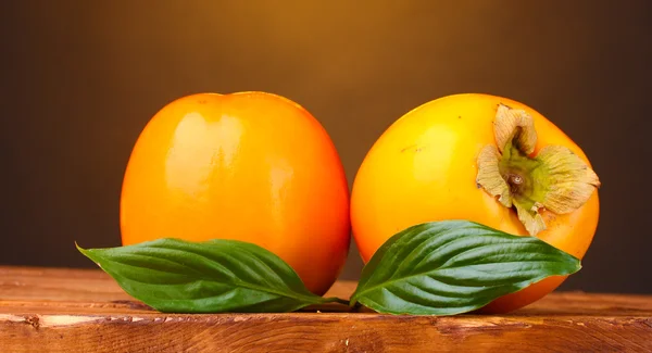 Deux persimmons appétissants sur table en bois sur fond marron — Photo