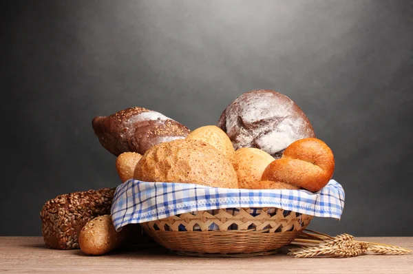 Delicious bread in basket and ears on wooden table on gray background — Stock Photo, Image