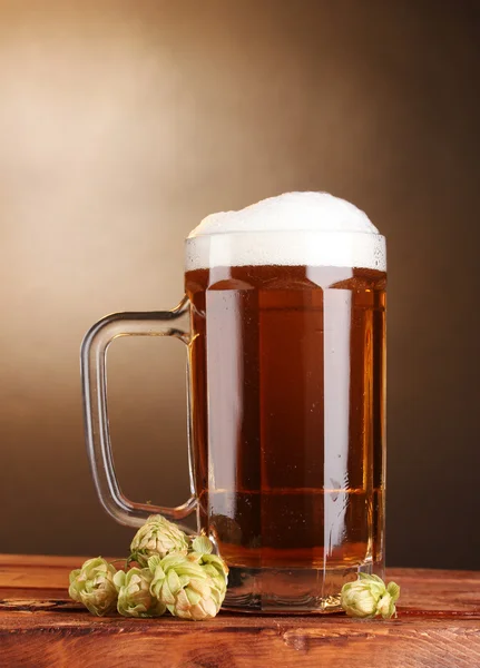 Caneca de cerveja e salto verde na mesa de madeira no fundo marrom — Fotografia de Stock