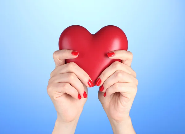 Rotes Herz in weiblichen Händen auf blauem Hintergrund — Stockfoto