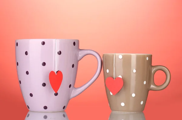 Duas xícaras e sacos de chá com rótulo vermelho em forma de coração no fundo vermelho — Fotografia de Stock