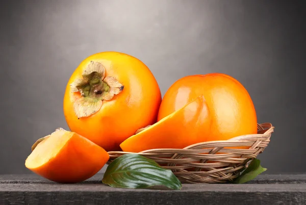 Appetizing persimmons in pad on wooden table on grey background — Stock Photo, Image