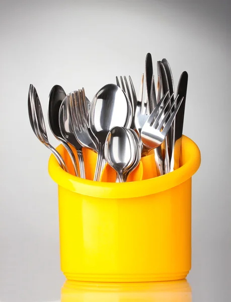 Cubertería de cocina, cuchillos, tenedores y cucharas en soporte amarillo sobre fondo gris —  Fotos de Stock