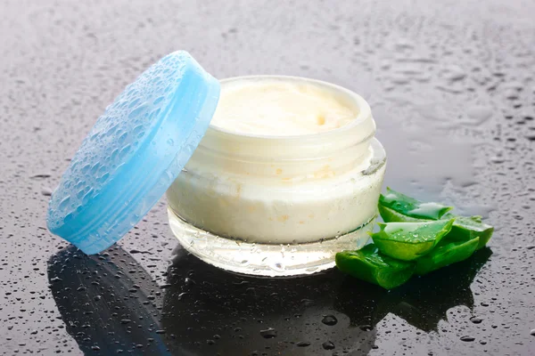 Opened glass jar of cream and aloe on black background with water droplets — Stock Photo, Image