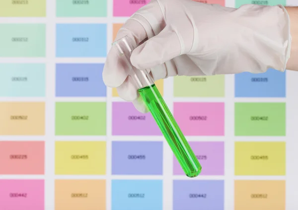 Tubo con líquido verde en la mano sobre el fondo de muestras de color —  Fotos de Stock