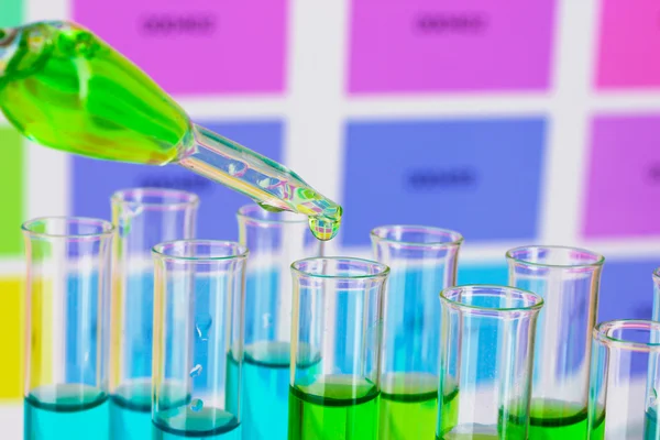 Test-tubes with color liquid and pipette on color samples background — Stock Photo, Image