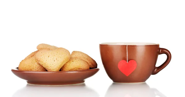 Tazza marrone con bustina di tè e biscotti a forma di cuore su piastra marrone isolato su — Foto Stock