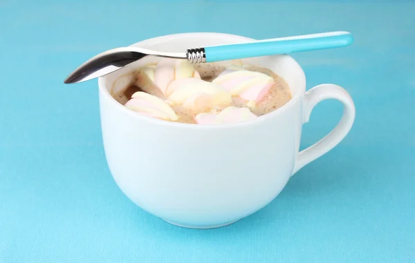 Xícara de cappucino com marshmallows e colher no fundo azul — Fotografia de Stock