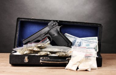 Cocaine, marijuana dollars and handgun in case on wooden table on grey back clipart