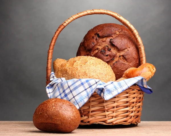 Leckeres Brot im Korb auf Holztisch auf grauem Hintergrund — Stockfoto