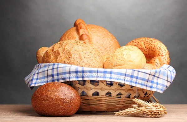 Delizioso pane in cesto e orecchie su tavolo di legno su sfondo grigio — Foto Stock