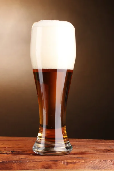 Bier in glas op houten tafel op bruine achtergrond — Stockfoto