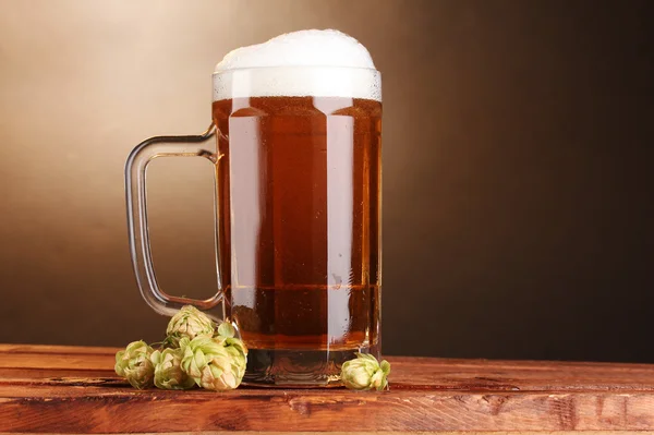 Jarra de cerveza y lúpulo verde sobre mesa de madera sobre fondo marrón — Foto de Stock
