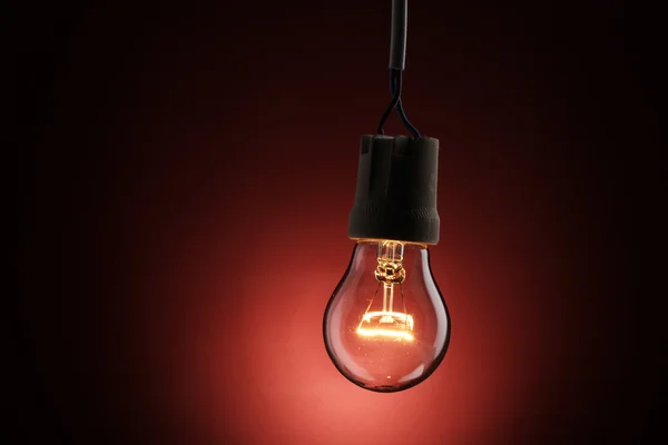 Eine beleuchtete Glühbirne auf rotem Hintergrund — Stockfoto