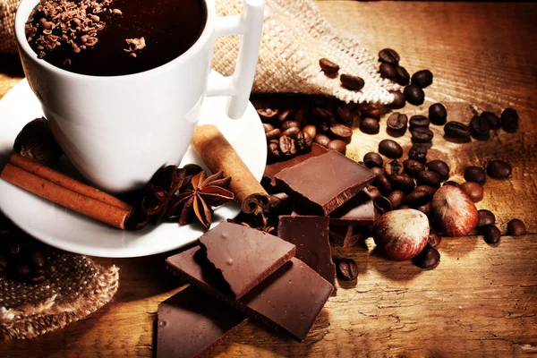 Чашка горячего шоколада, палочки корицы, орехи и шоколад на деревянном столе — стоковое фото