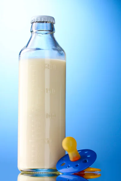 Bottle of milk and soother on blue background — Stock Photo, Image