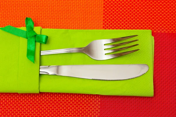 Forchetta e coltello in panno verde con fiocco su tovaglia rossa — Foto Stock