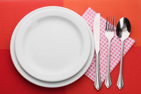 Beyaz boş tabak çatal, kaşık ve bıçak üzerinde kırmızı bir masa örtüsü — Stok fotoğraf