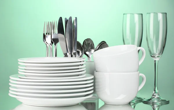 Platos limpios, vasos, vasos y cubiertos sobre fondo verde —  Fotos de Stock