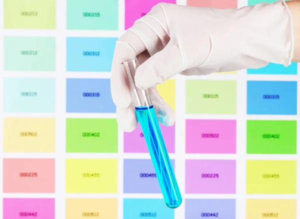 Tube avec liquide bleu à la main sur fond d'échantillons de couleur — Photo