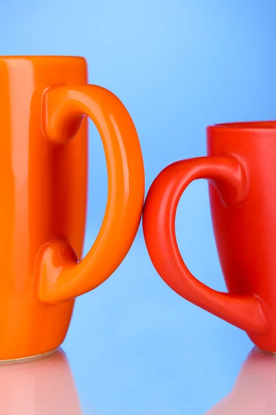 Duas xícaras coloridas alças close-up no fundo azul — Fotografia de Stock