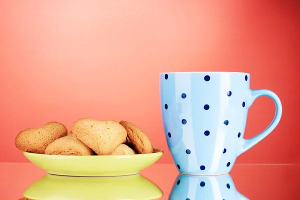 Heart-shaped cookies on plate and cup on red background — Stock Photo, Image