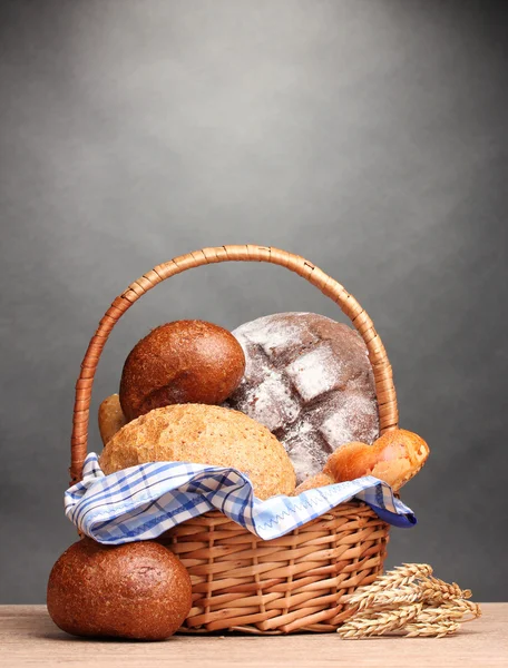 Вкусный хлеб в корзине и уши на деревянном столе на сером фоне — стоковое фото