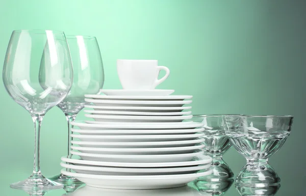 Clean plates, cup and glasses on green background — Stock Photo, Image