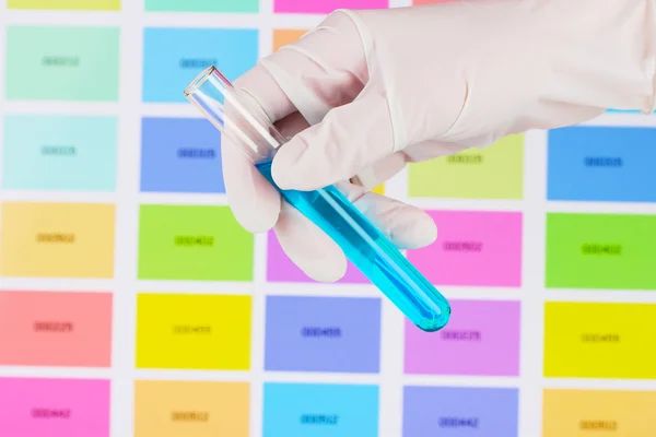 Tube with blue liquid in hand on color samples background — Stock Photo, Image