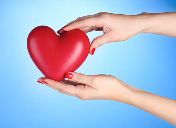 Czerwone serce w ręce kobiety na niebieskim tle — Zdjęcie stockowe