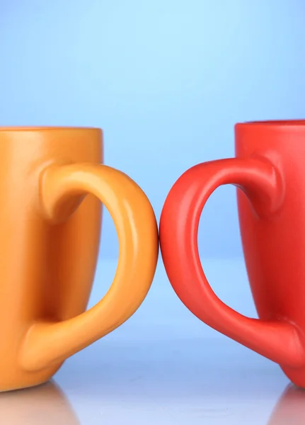 Due tazze colorate maniglie primo piano su sfondo blu — Foto Stock