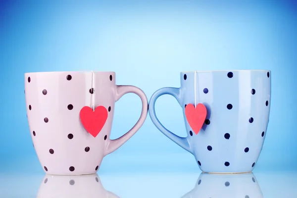 Dva šálky a čajové sáčky s červeným štítkem ve tvaru srdce na modrém pozadí — Stock fotografie