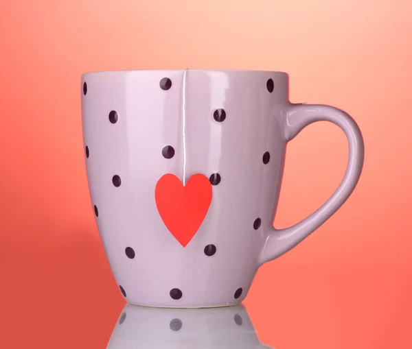 Roze cup en theezakje met rood hart-vormige label op rode achtergrond — Stockfoto