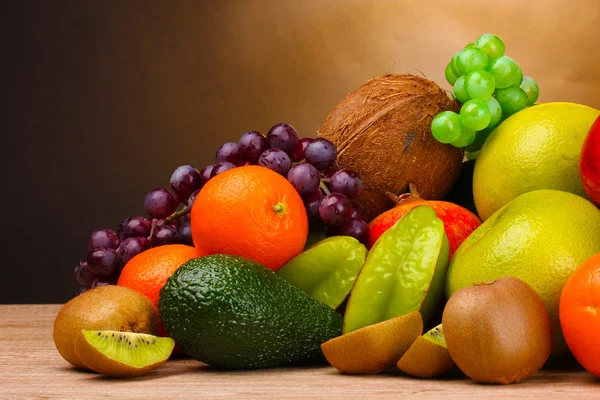 Assortment of exotic fruits on wooden table on brown background — Stock Photo, Image