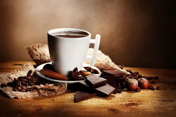 Cup of hot chocolate, cinnamon sticks, nuts and chocolate on wooden table o — Stock Photo, Image