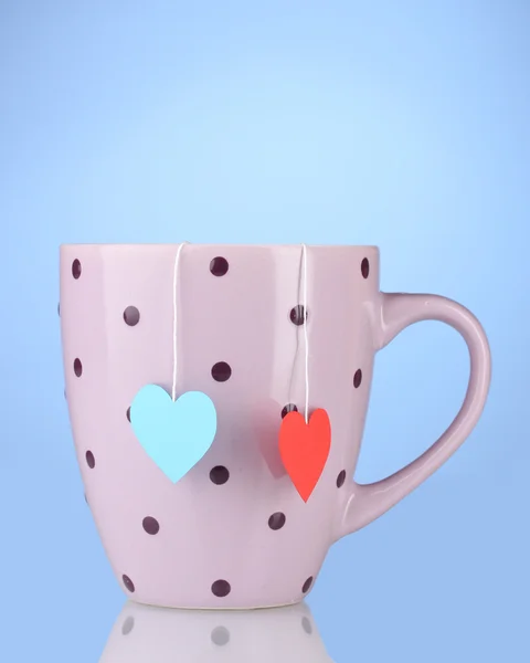 Růžové cup a dvě čajové sáčky s červené a modré srdce tvarovaný štítek na modré zpět — Stock fotografie