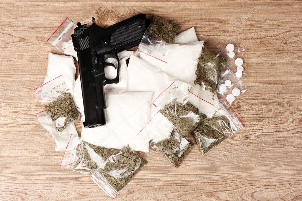 Cocaine and marihuana in packages and handgun on wooden background