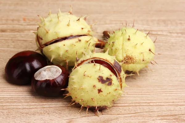 Green and brown chestnuts on wooden background — Stock Photo, Image