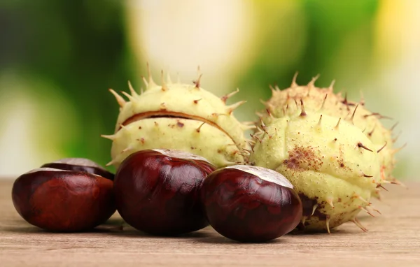 Green and brown chestnuts on wooden table on green background — Stock Photo, Image