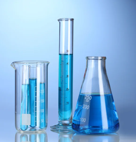 Laboratorieartiklar av glas med blå vätska med reflektion på blå bakgrund — Stockfoto