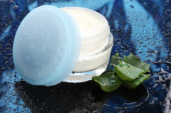 Frasco de vidrio abierto de crema y aloe sobre fondo azul oscuro con gota de agua — Foto de Stock