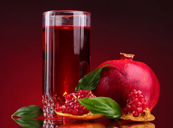 stock image Ripe pomergranate and glass of juice on red background
