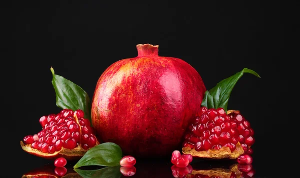 Ripe pomegranate fruit with leaves on black background — Stock Photo, Image