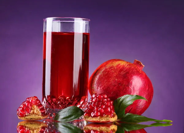 Rijpe pomergranate en glas sap op paarse achtergrond — Stockfoto