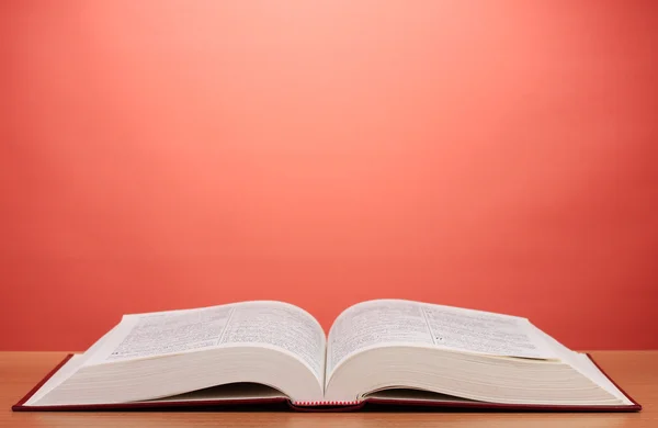 Öppna bok på träbord på röd bakgrund — Stockfoto