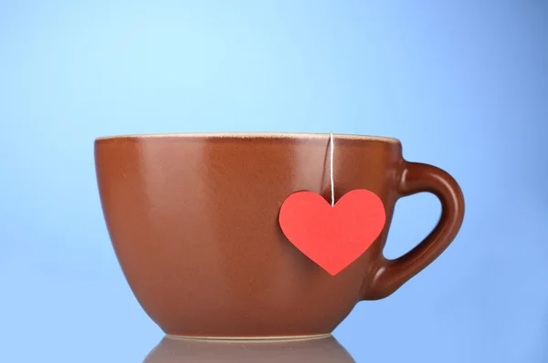 Taza marrón y bolsa de té con etiqueta roja en forma de corazón sobre fondo azul —  Fotos de Stock
